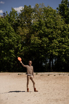 Man throws orange frisbee in park with trees and blue sky