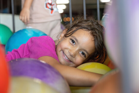 Happy girl smiles while playing in colorful giant ball pit