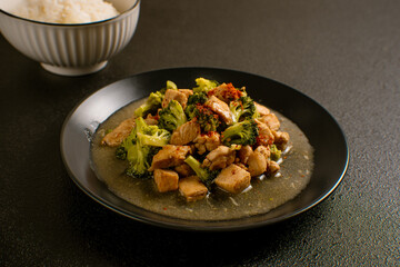 Delicious stir-fried chicken with broccoli served on a black plate with chopsticks and sauce, Asian homemade cuisine. Perfect for recipes, articles or any cooking content.
