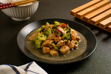 Delicious stir-fried chicken with broccoli served on a black plate with chopsticks and sauce, Asian homemade cuisine. Perfect for recipes, articles or any cooking content.
