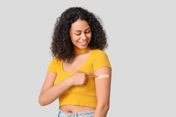Beautiful young happy African-American woman pointing at applied medical patch on grey background