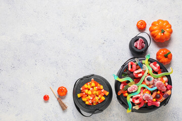 Composition with pots of tasty candies for Halloween and decorative pumpkins on light background