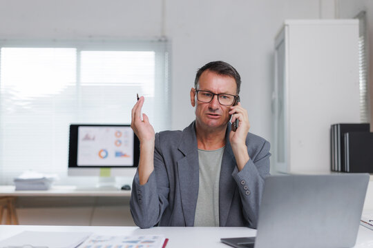Mature businessman having frustrating phone conversation in office