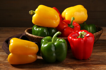 Wicker bowl with fresh colorful bell peppers on wooden background