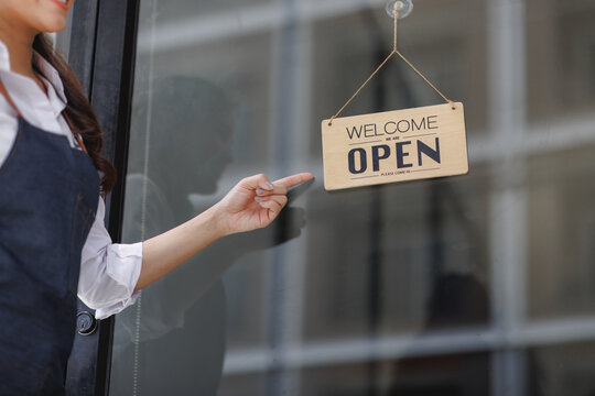 Business owner pointing welcome open sign on door - Powered by Adobe