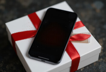 Smartphone with Merry Christmas message on gift box with red ribbon on dark background.