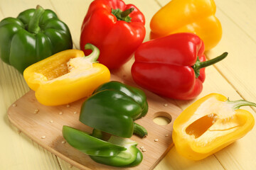 Cutting board with fresh colorful bell peppers on yellow wooden background, closeup