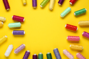 Frame made of colorful thread spools on yellow background