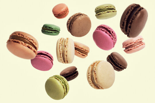 Variety of multicolored macarons falling in midair against pale green background
