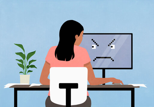 Woman working at computer with angry face on screen
