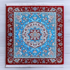 Intricate square rug with red floral border, light blue center, on white wood