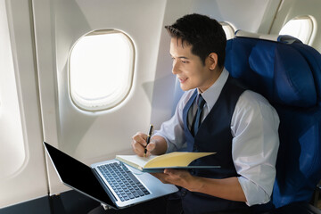 Fototapeta premium Traveling and technology. happy young businessman working on laptop computer and smartphone while sitting in airplane.