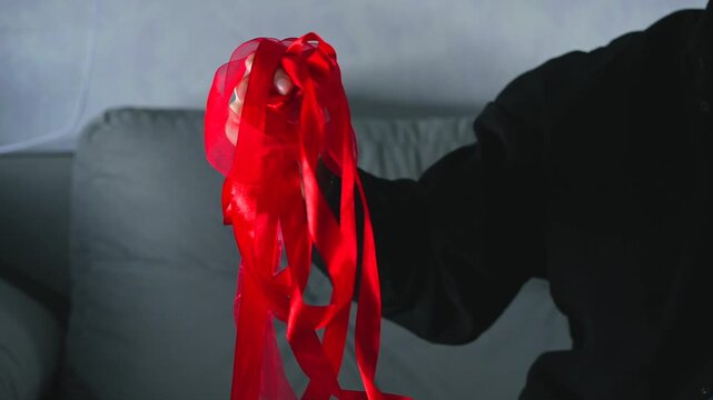 A man holds a long, tangled red satin ribbon and can't untangle it.
Close-up of an untangled skein of red satin ribbon.
