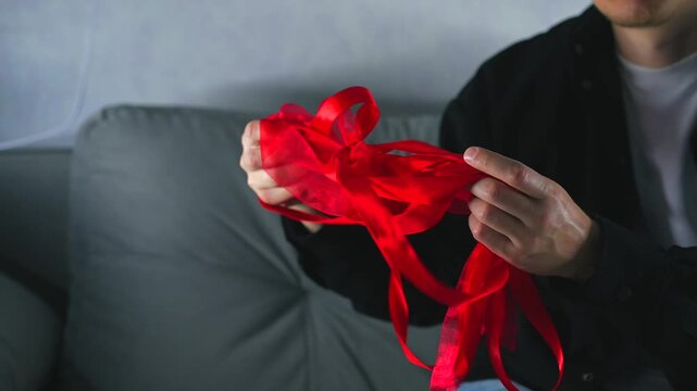 A man holds a long, tangled red satin ribbon and can't untangle it.
Close-up of an untangled skein of red satin ribbon.