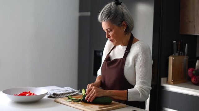Senior woman cutting fresh cucumber for salad