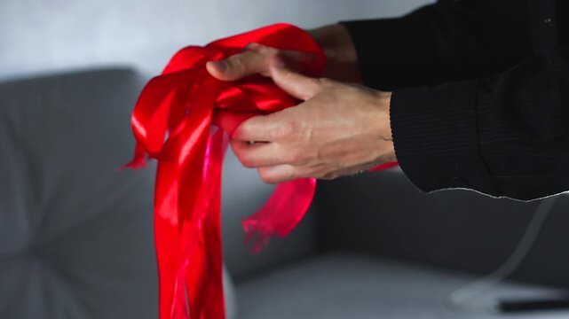 A man holds a long, tangled red satin ribbon and can't untangle it.
Close-up of an untangled skein of red satin ribbon.
