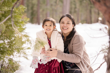 Woman and child smile brightly in snowy Tahoe forest clearing