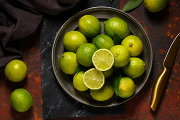 Plate with fresh ripe limes on dark background