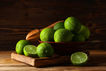 Bowl and board with fresh ripe limes on wooden background