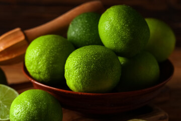 Bowl with fresh ripe limes and juicer on wooden background, closeup