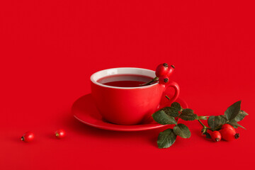Cup of hot rose hip tea and berries on red background