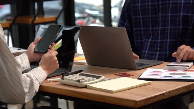 Business Collaboration: Two individuals engage in collaborative work, utilizing technological tools like a phone and laptop to facilitate effective teamwork and data analysis. 