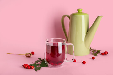 Glass cup of hot rose hip tea and berries on pink background