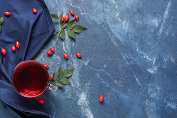 Glass cup of hot rose hip tea and berries on blue background