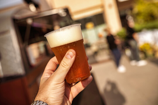 Hand holding plastic cup of craft beer outdoor - Powered by Adobe