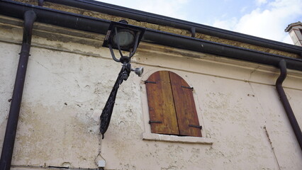 An antique wrought iron street light fixture and a small, closed wooden window shutter on the...