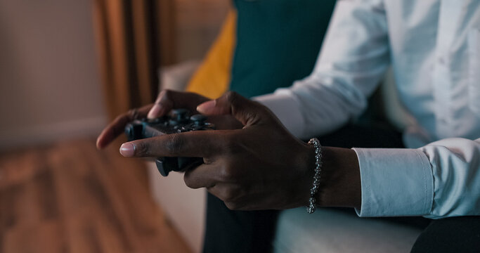 A close-up of the hands of a student wearing a bracelet and a ring, quickly pressing buttons on a game controller. He is actively playing a console game, dressed in a white shirt.