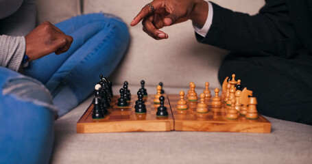 A close-up of a chessboard placed on a sofa with pieces arranged for play. Two friends of...