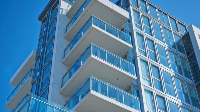 Modern apartment building with glass balconies and windows under blue sky background