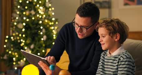 During Christmas evening, a father teaches his child by reviewing toy instructions on a tablet....