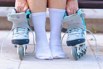 Close up of roller skates on the ground with person wearing white socks, sitting outdoors and...