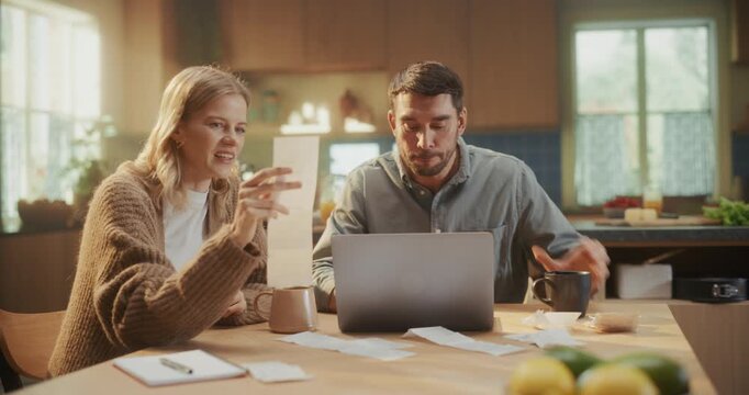 Man and Woman Working on Personal Accounting Together at the Kitchen Table at Home. Female Checks Paperwork and Invoices as Male Inputs Numbers into a Laptop Computer Spreadsheet