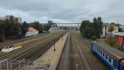Naklejka premium Railway tracks with a blue train under a cloudy sky in urban area 
