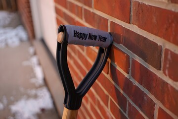 Shovel with happy new year text leaning on a brick wall