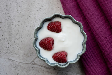 Green porcelain bowl and natural yogurt with red berries on the wood table.