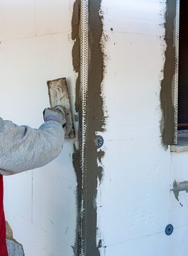 Builder applying the base coat of mortar over the fiberglass mesh on external thermal insulation (ETICS) system, showing energy efficiency work on a new home construction site.