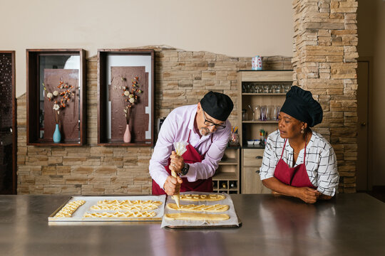 Experienced baker piping filling onto pastry dough while apprentice watches
