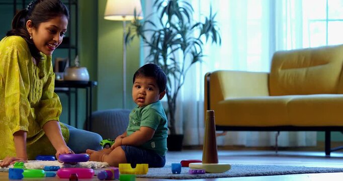 Indian infant boy crawling on carpet with young mother nearby in modern living room, sharing joyful moments, love, affection, bonding, and nurturing early childhood development indoors