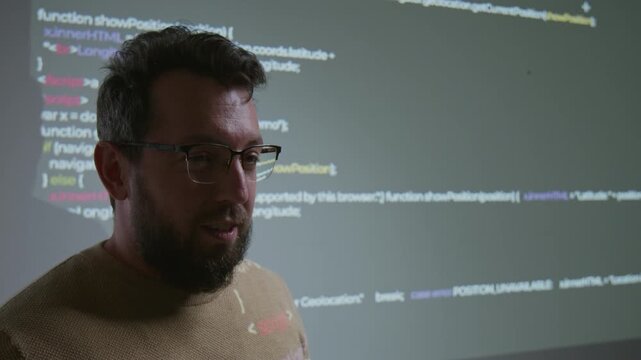 Close-up of face of Caucasian male coding teacher demonstrating computer web design script projected on wall, while conducting lecture for students at college or university