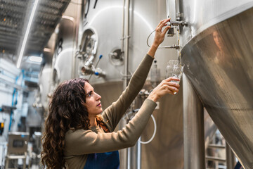 Woman brewer drawing beer from a fermentation tank for quality control, working in a craft beer production facility