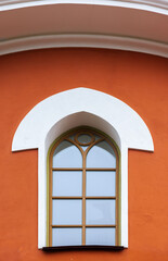 Fototapeta premium Bright orange building facade features a white rounded arch and a tall arched window