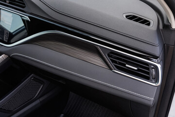 Modern car dashboard featuring wood grain accent, chrome air vent and stitched soft-touch surfaces