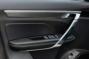 Modern car door panel with black stitched leather, metallic handle and integrated control buttons