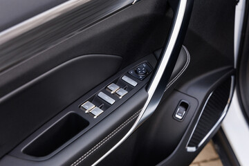 Driver-side car door panel with power window switches, mirror adjustment pad and metallic handle