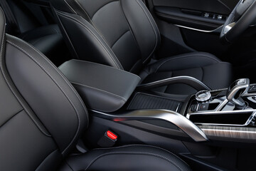 Front car seats in black leather with stitching, rotary dial, gear shifter and red seatbelt latch