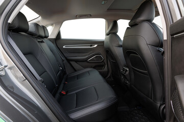Backseat view of modern car interior with black leather seats, white stitching, geometric door accents and rubber mats